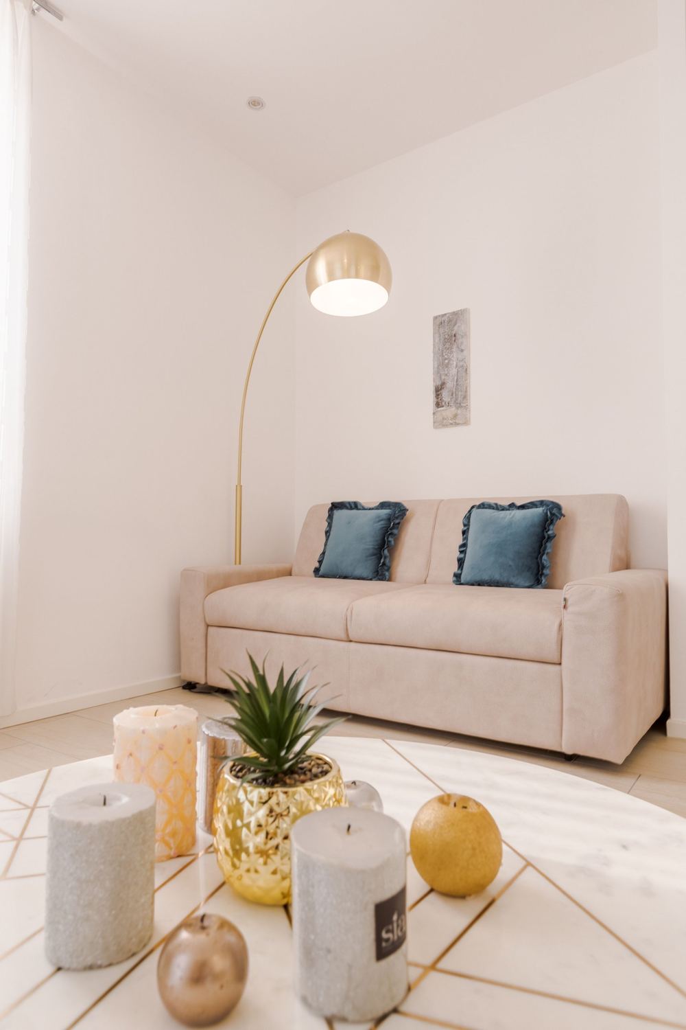 Sala con paredes blancas, sofá beige, lámpara de arco dorada y mesa de centro